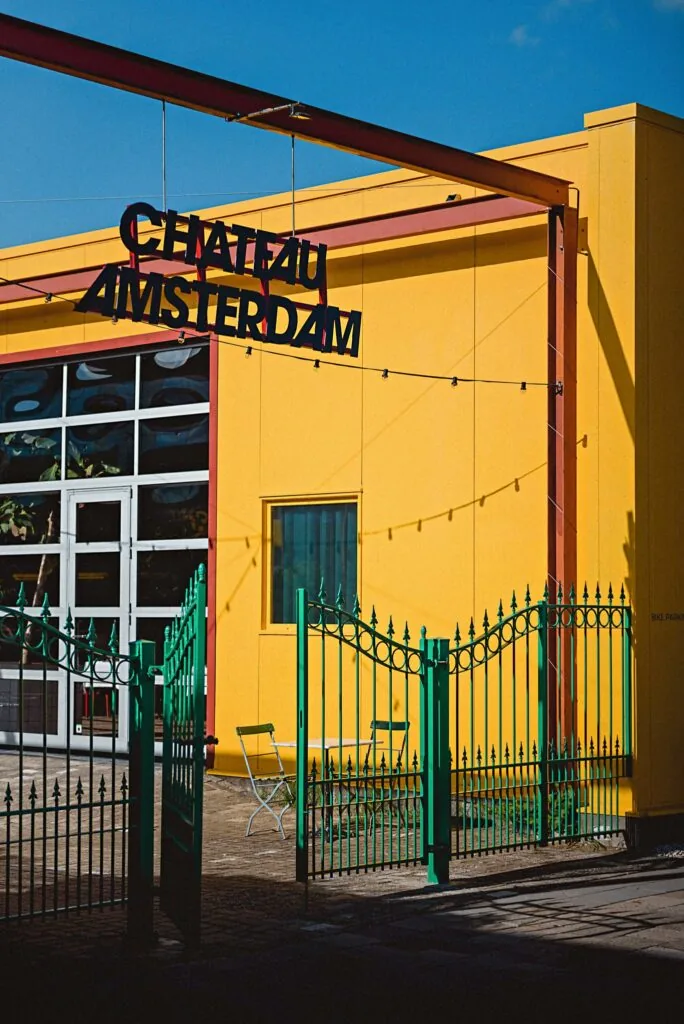 Geel gebouw met opschrift “Chateau Amsterdam” en een groene toegangspoort aan de Johan van Hasseltweg.